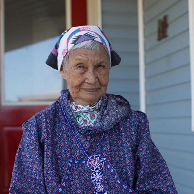 A woman wearing traditional, colorful clothing sits in front of a red door.